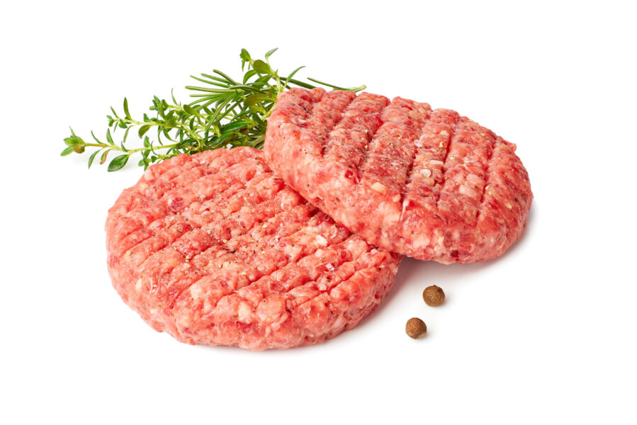 Two raw burger patties with thyme and reosemary on white Meat